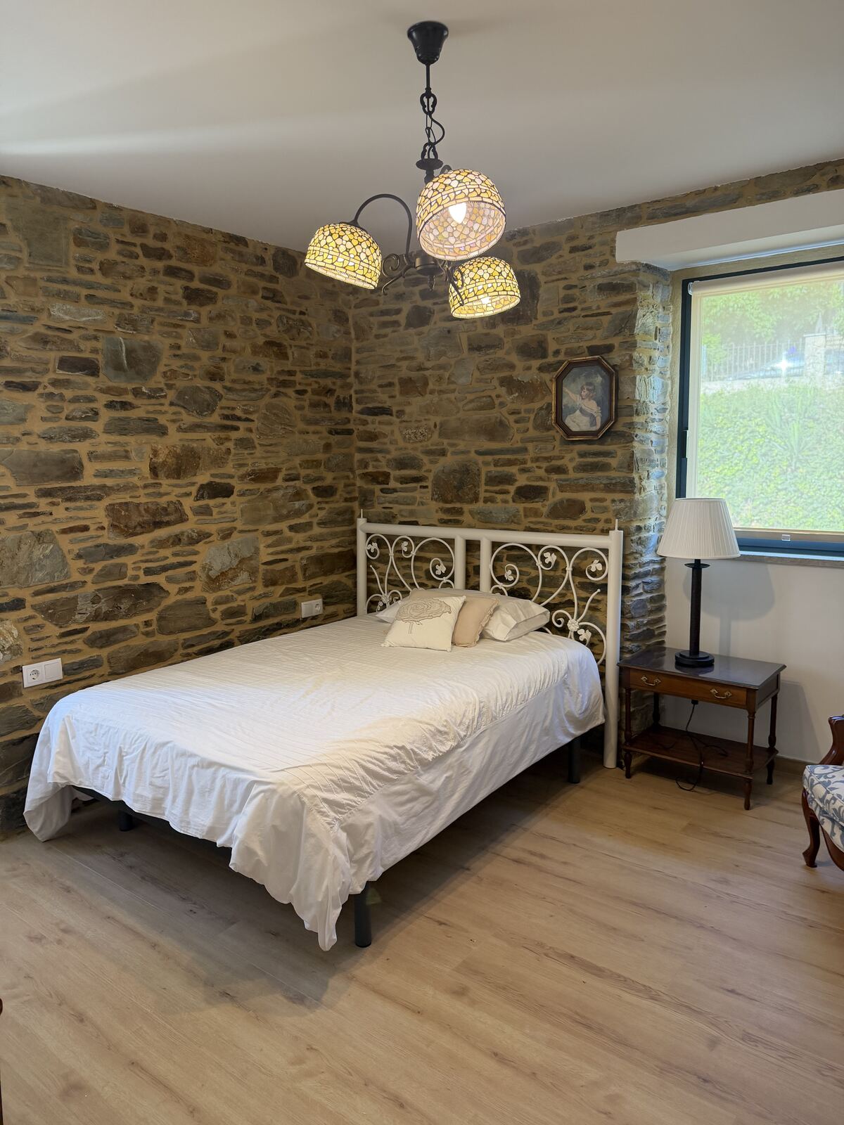 Tercera habitación con cabecero de forja blanca y muro de piedra